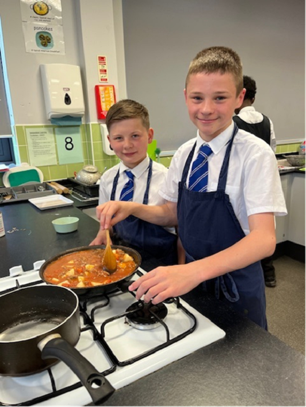 Two young male students cooking an aromatic beef and potato curry in a pan on a hob.