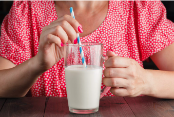 Woman about to drink a glass of milk with a straw.