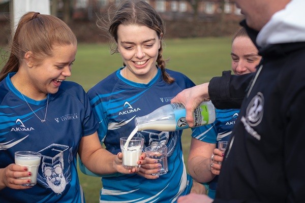 Three female rugby players holding glasses of milk.
