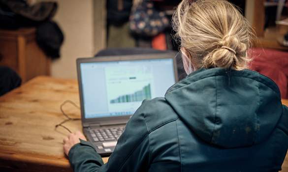 Woman sat at a table typing on a laptop.