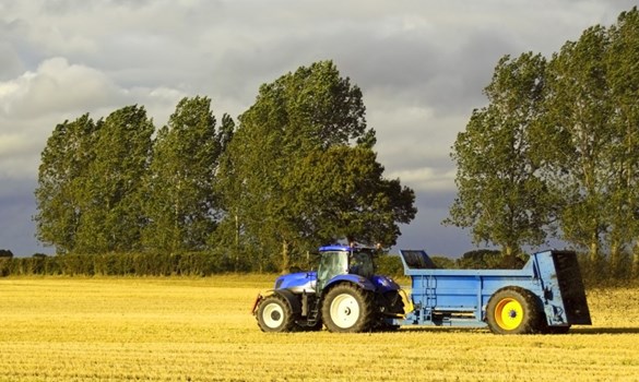 a blue tractor spreading manure on a stubble field