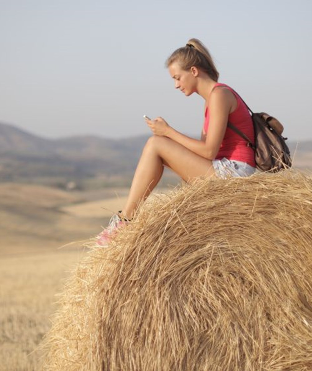 A young woman sitting on a bale of hay in a field.