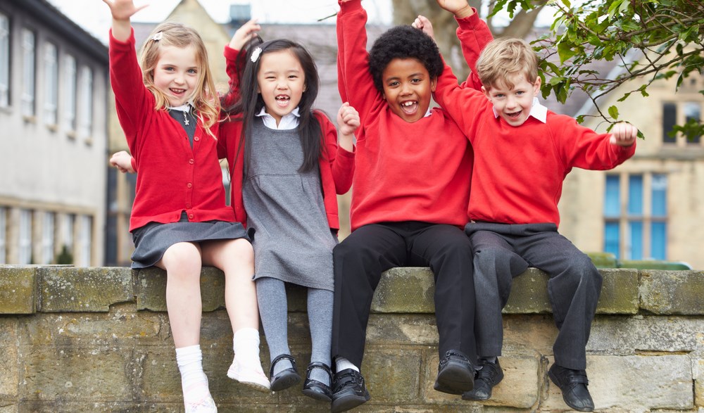 Happy children in school uniform sitting on wall with arms in the air