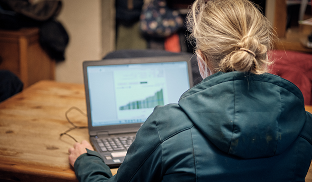 Woman sat at a table typing on a laptop.